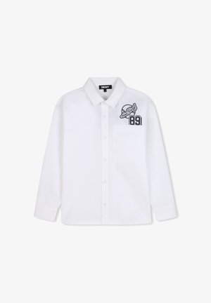 Chemise blanche à manches longues boutonnée avec poche avant et logo noir "New York 89" sur le côté supérieur gauche, étiquette DKNY à l'intérieur du col.