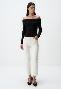 Zwarte off-shoulder top met geribbelde textuur, gecombineerd met witte rechte jeans. Het model draagt zwarte hoge hakken. Eenvoudig, schoon ontwerp.