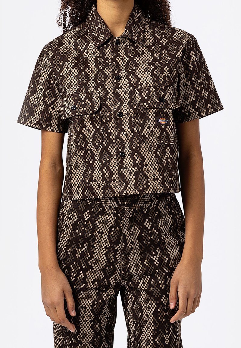 Personne portant une chemise à manches courtes boutonnée assortie et un pantalon avec un motif peau de serpent marron et beige et des poches avant.