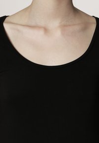 Juodas prigludęs viršus su plačiu apvaliu iškirpimu, pagamintas iš minkštos medžiagos. Lygus paviršius su minimaliais siūlais. Nematyti jokių dekoracijų ar raštų.