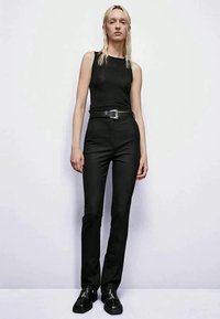 Un haut sans manches noir associé à un pantalon noir ajusté. Présente une coupe slim, un tissu texturé et une boucle de ceinture en argent. Des chaussures noires complètent le look.