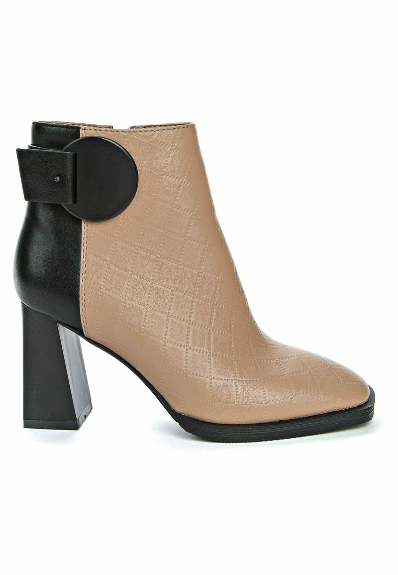 Botín beige de tacón con textura acolchada, tacón negro y detalle circular. Presenta punta puntiaguda y acabado en cuero liso.