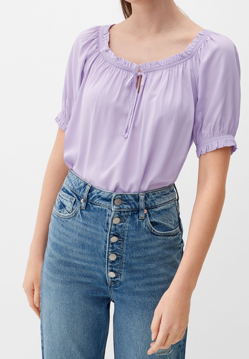 Lavender blouse with a square neckline and drawstring detail; short puffed sleeves; paired with high-waisted blue denim jeans featuring button front.