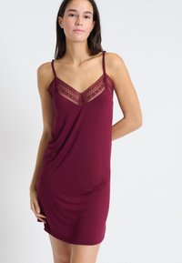 Burgundowa nocna koszula z koronkowym wykończeniem przy dekolcie, cienkimi regulowanymi ramiączkami, miękkim materiałem i swobodnym fasonem opadającym do połowy uda.