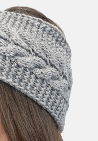 Diadema de punto gris con un patrón trenzado, textura suave y un ajuste ceñido, diseñada para cubrir las orejas.