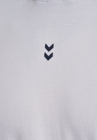 White cotton t-shirt featuring a small navy blue emblem of two downward-facing chevrons on the front. Soft texture, crew neck design.
