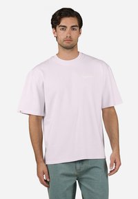 Helles rosa, übergroßes Baumwoll-T-Shirt mit Rundhalsausschnitt und kurzen Ärmeln, das ein kleines, bedrucktes Logo auf der Brust trägt.