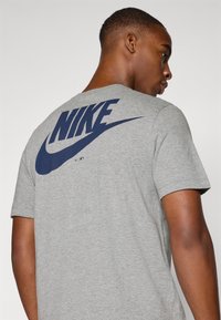 Pilkas medviln�ės marškinėlis su dideliu tamsiai mėlynu Nike logotipu ant nugaros. Trumpomis rankovėmis, apvali iškirptė ir švelni tekstūra.