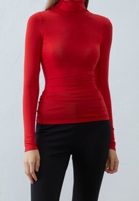 Rød langærmet turtleneck-top lavet af et blødt, strækbart stof, med en tætsiddende silhuet og glat tekstur, parret med sorte bukser.