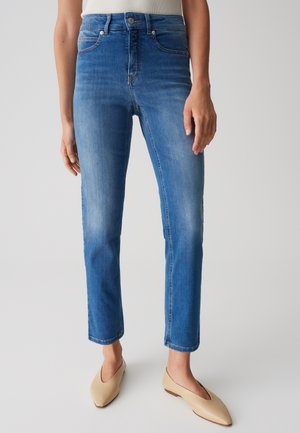 Jeans in denim blu con taglio dritto, caratterizzati da vita alta, cinque tasche e leggera sbiaditura. Abbinati a ballerine beige con punta appuntita.