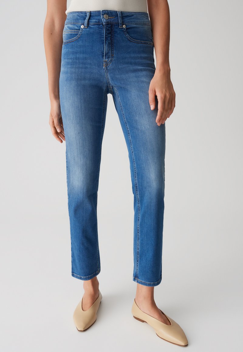 Jeans in denim blu con taglio dritto, caratterizzati da vita alta, cinque tasche e leggera sbiaditura. Abbinati a ballerine beige con punta appuntita.