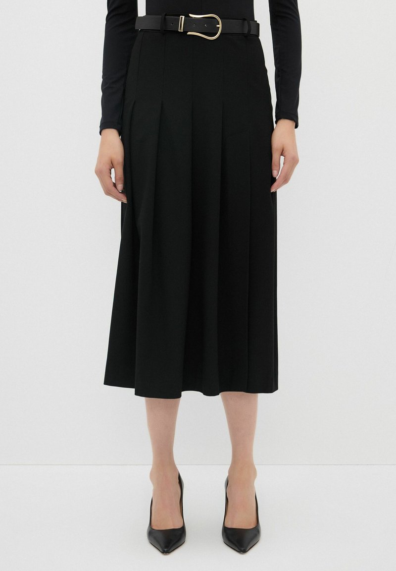 Falda negra con pliegues y cinturilla ancha, con una hebilla dorada. Tela suave y corte en A, complementada con elegantes tacones altos negros.