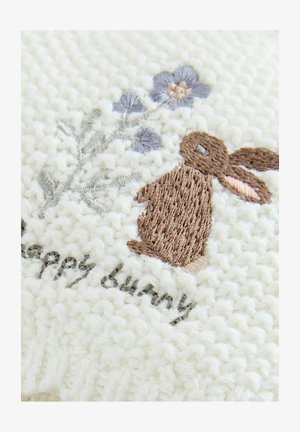 Strikket stof i creme farve har en broderet brun kanin med syede blomster og teksten "glad kanin" i grå tråd, som viser tekstur og detaljer.