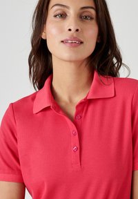 Polo shirt rosa brillante con colletto, maniche corte, patta con tre bottoni e texture a coste. Adatto per un uso informale.