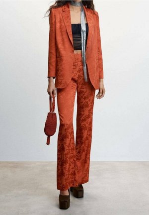 Rood colbert en broek met bloemmotief, gecombineerd met een zwarte crop top. Gecompleteerd met plateauhakken en een kleine gestructureerde handtas.