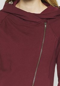 Bordeaux hætte sweatshirt med cowl-neck, udstyret med en diagonal lynlås og synlige søm detaljer. Blød, glat stof tekstur.