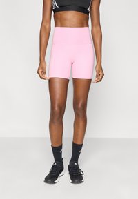 Ροζ αθλητικά σορτς με ψηλή μέση και πλαϊνές ραφές, κατασκευασμένα από λείο ύφασμα. Φοριούνται με μαύρα αθλητικά παπούτσια και κάλτσες για ολοκληρωμένη εμφάνιση.