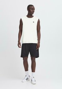 Canotta beige chiaro senza maniche con scollatura rotonda, abbinata a pantaloni corti neri. Sneakers bianche con strisce nere. Design semplice e casual.