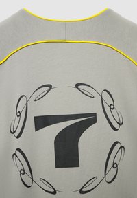 Indumento grigio con il numero 7 stilizzato in nero, centrato e circondato da vortici astratti neri simmetrici e bordini gialli lungo il colletto.