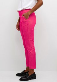 Pantaloni rosa su misura a vestibilità slim con tasche laterali, caratterizzati da una texture liscia e una leggera lucentezza, abbinati a mocassini neri.