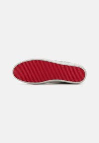 Suola di scarpa in gomma con un design testurizzato e rigato in rosso. I bordi sono lisci e la soletta è bianca con una leggero curvatura.