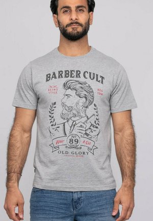 Homme portant un T-shirt gris avec une illustration vintage de barbier et les textes « BARBER CULT », « Hair & Cut » et « Old Glory » à l'avant.