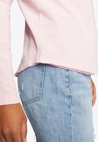 Helles rosa Langarmshirt mit ausgefranstem Saum, kombiniert mit distressed hellblauen Denim-Shorts, die eine Tasche und eine lässige Passform bieten.