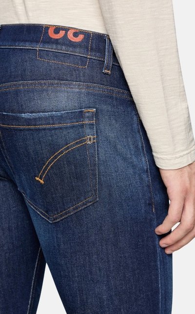 Jeans in denim blu scuro con un design a tasca posteriore curvato e cuciture arancioni a contrasto, indossati con una maglietta a maniche lunghe di colore chiaro.