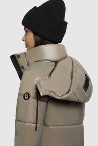 Giubbotto imbottito beige, con colletto alto, tasche con zip e dettagli neri. Il materiale ha una texture liscia e lucida.