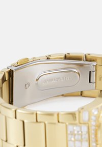 Bracelet de montre en acier inoxydable doré avec un fermoir argent poli. Caractéristiques des maillons rectangulaires et une texture lisse, avec des détails gravés sur le fermoir.
