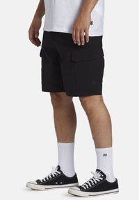 Sorte cargo shorts med sidelommer, lavet af holdbart stof. Kombination med sorte sneakers og hvide ankelsokker. Enkel og funktionel design.