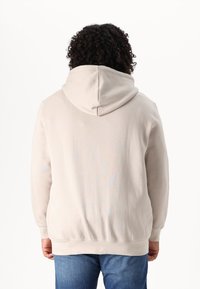Lichtbeige hoodie met een trekkoord in de capuchon, ribbelmanchetten en -zoom. Zachte textuur, eenvoudig ontwerp, gecombineerd met blauwe jeans.