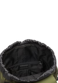 Vue de dessus d'un sac à dos vert à cordon ouvert montrant une doublure intérieure noire, une poche zippée et deux compartiments plus petits à l'intérieur.