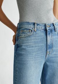 Ljusblå denimjeans med en klassisk femficksdesign, blekt utseende och guldtråd vid sömmarna och knapplåsningen.