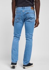 Jasnoniebieskie dżinsy z pięcioma kieszeniami, skórzaną łatą z tyłu i kontrastowymi szwami. Slim fit z prostą nogawką.