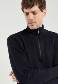 Granatowy sweter z dzianiny o fakturowej strukturze, z wysokim kołnierzem i pół zamkiem. Dopasowany krój, długie rękawy oraz prążkowane detale.