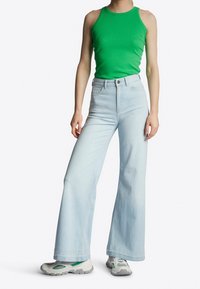 Lys blå, vide jeans parret med en tætsiddende grøn tanktop; tekstureret stof; afslappede sneakers med grå og grønne detaljer.