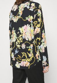 Camicia nera a maniche lunghe con motivo floreale, caratterizzata da fiori colorati, farfalle e accenti dorati, dal tessuto morbido e con orlo curvo.