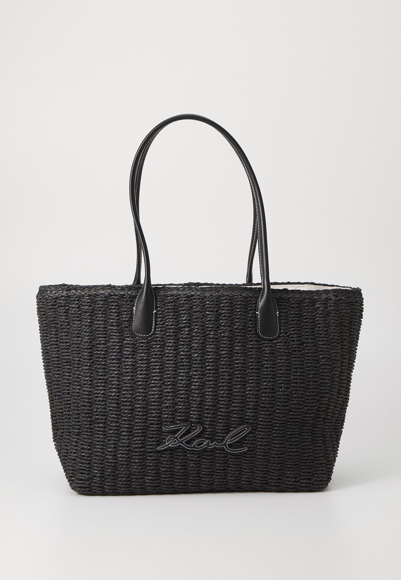 Black woven tote bag with leather handles, featuring a textured surface and embroidered logo detail on the front.