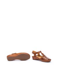 Sandali in pelle marrone con design a taglio, cinturino regolabile e suola in gomma texturizzata. L'altezza del tacco è moderata per garantire comfort.