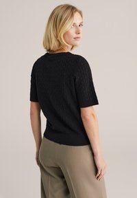 Čierny krátky rukáv sveter s textúrovaným geometrickým vzorom, rebrovaným výstrihom a lemom, skombinovaný so svetlošedými širokými nohavicami.