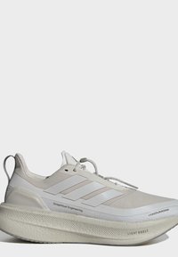 Vaalean beige Adidas Ultraboost juoksukengät, joissa paksu pehmustettu pohja, kolme raitaa sivulla ja vetosilmukka kantapäässä.