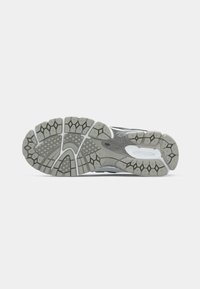 Semelle d'une chaussure de sport grise et blanche avec des motifs de bande de roulement hexagonaux et rectangulaires et des rainures flexibles.