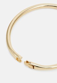 Bracelet en métal doré avec une finition lisse et polie. Présente un design ouvert avec un fermoir sécurisé à une extrémité.