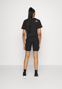 Svart kortärmad t-shirt och svarta shorts, båda i ett mjukt material. Kombineras med svarta sneakers och strumpor med blå ränder. Enkelt design, inga mönster.