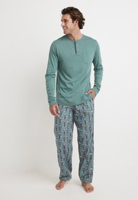 Turquoise lange mouwen shirt met een henley halslijn en zak, gecombineerd met gestreepte pyjamabroek met kleurrijke nutcracker motieven.
