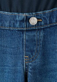 Zbliżenie na pas niebieskich dżinsów z widocznym przeszyciem, metalowym guzikiem i dziurką na guzik na tle ciemnej tkaniny.