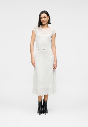 Biała prążkowana sukienka midi z dekoltem w łódkę, dopasowanym gorsetem i falbankowym dołem, podkreślona cienkim paskiem. Noszona z czarnymi botkami za kostkę.