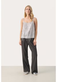 Srebrny tank top z cekinami i pionowym wykończeniem frędzlami, w połączeniu z szarymi spodniami typu wide-leg i srebrnymi balerinami, na neutralnym tle.