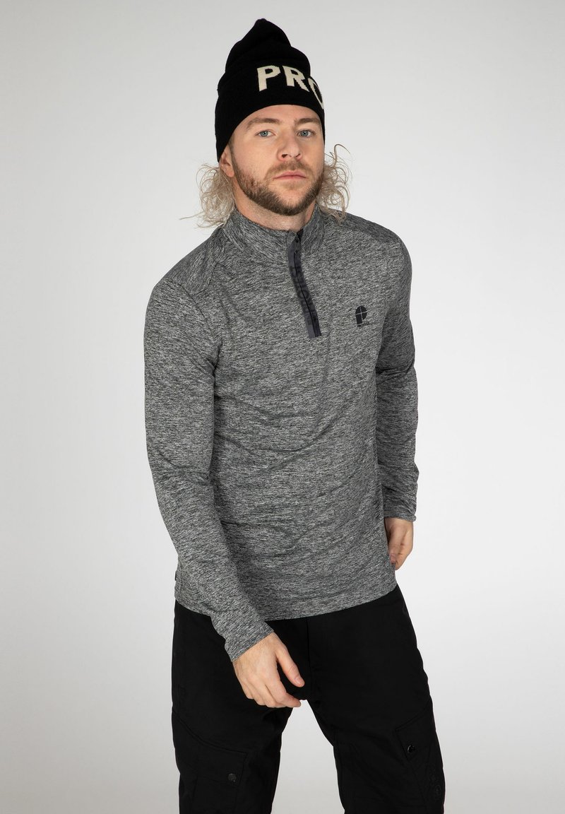 Suéter gris de manga larga con cuello con cremallera y acentos negros, combinado con pantalones cargo negros. La tela tiene un patrón texturizado.